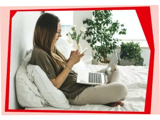 Woman using laptop and phone on a bed