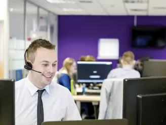 Man smiling at his desk, wearing a headset